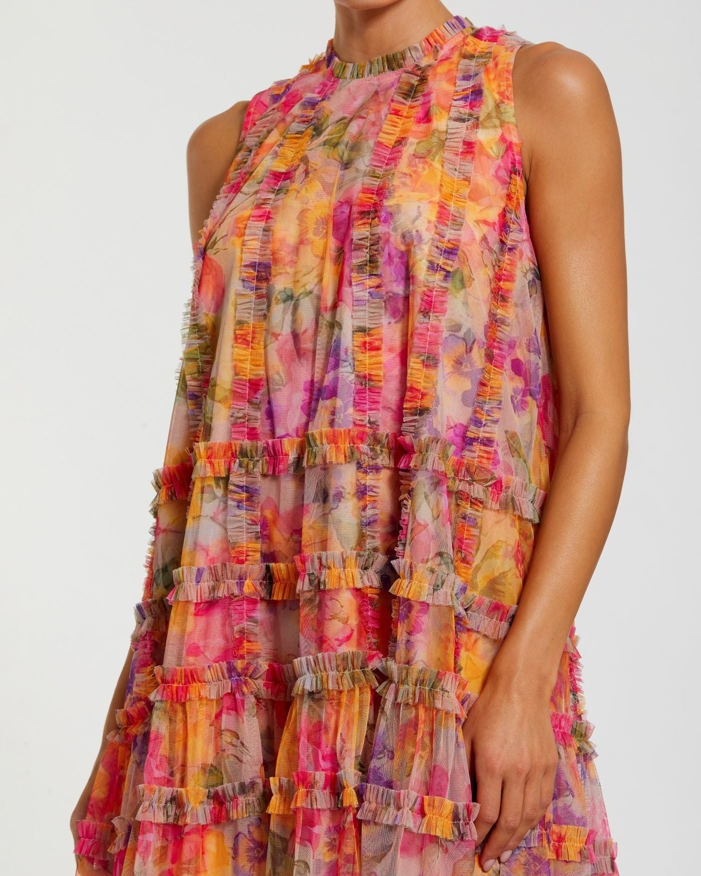 A person wearing the Mac Duggal 8488 Short Party Dress, a sleeveless mini party dress featuring a multicolored floral design with ruffle accents and tiered layers, shown from shoulders to mid-thigh.